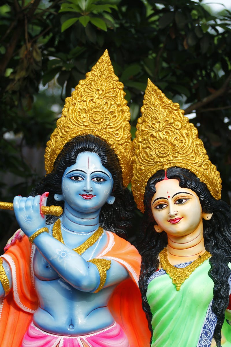 Vibrant sculptures of Krishna and Radha with intricate details set against a lush garden backdrop.