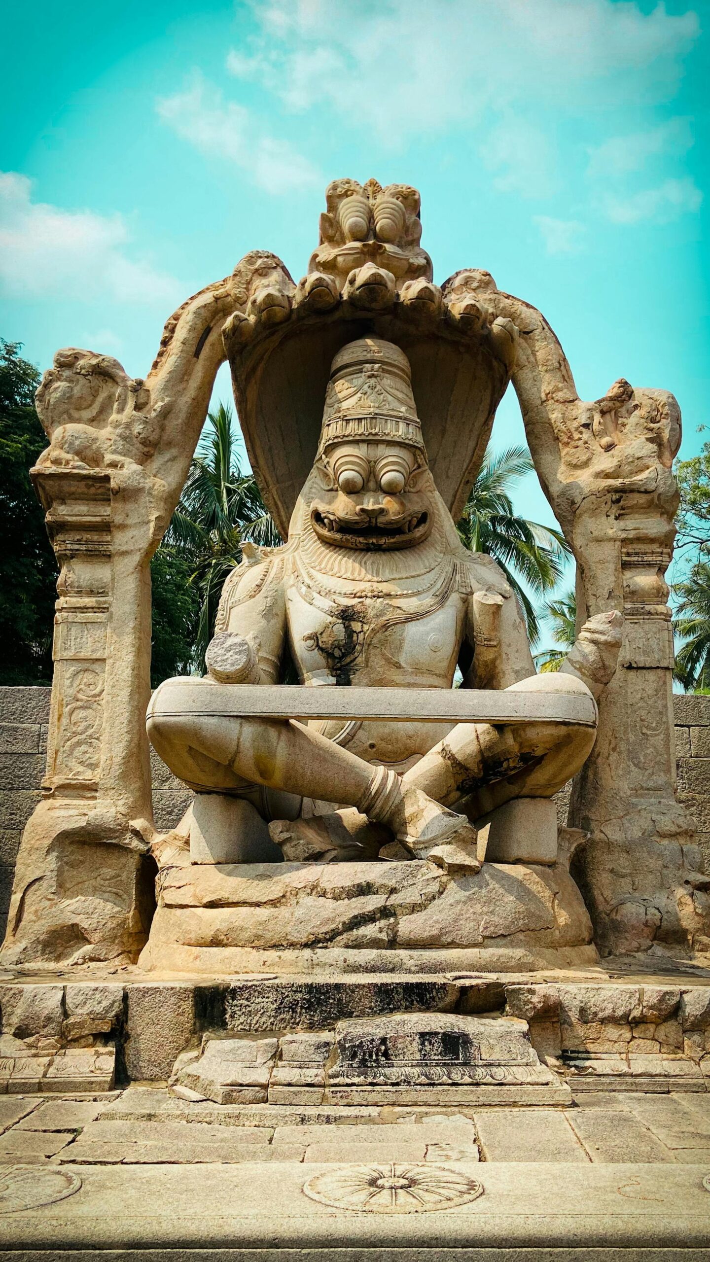 Ancient Narasimha statue at Hampi, India, showcasing intricate stone carvings under a clear blue sky.