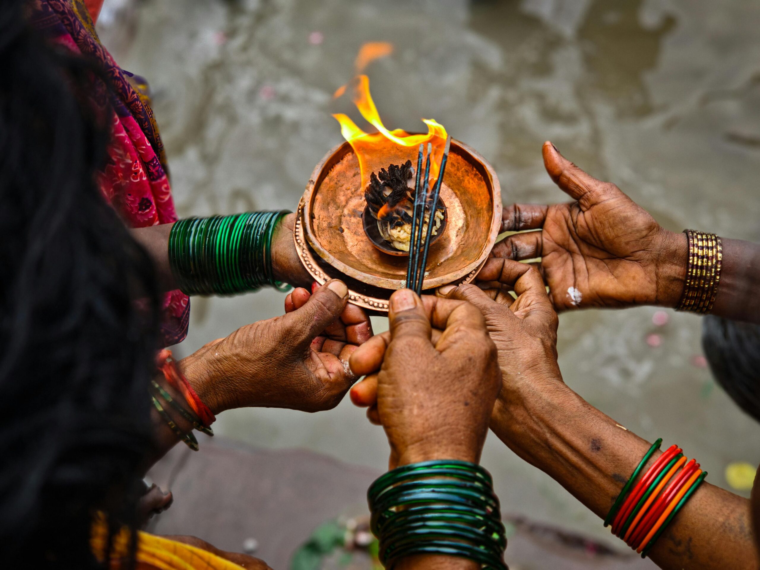 Vibrant Indian ritual scene with hands holding a burning offering near river.