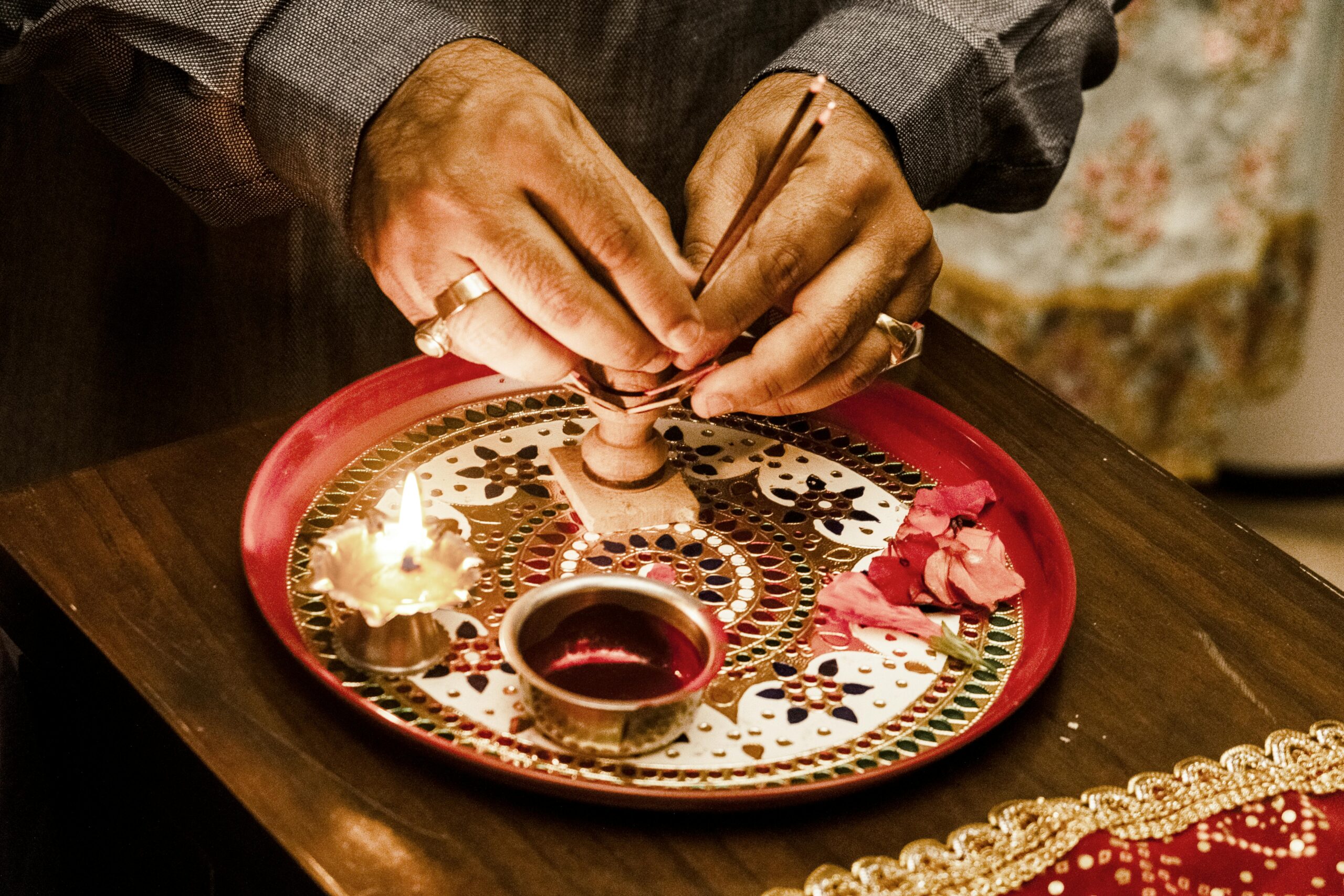 Close-up of a person lighting incense sticks on a decorated tray for a traditional Indian ritual.